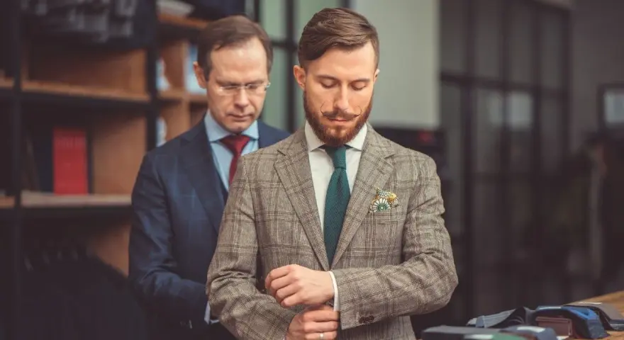 Elegancki garnitur dla świadka, dopasowywany przez krawca. Mężczyzna z wąsikiem przymierza tweedową marynarkę w kratę.