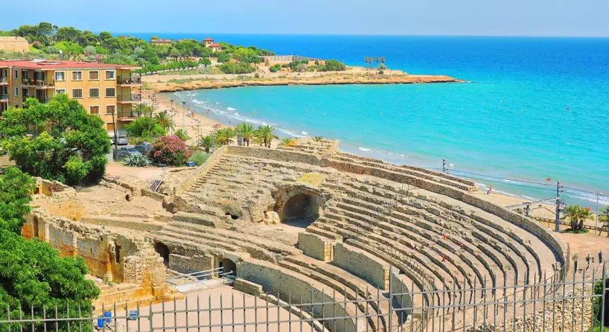 Ancient Roman amphitheater ruins overlooking a beautiful beach and turquoise sea. Discover Tarragona things to do, from history to relaxation.