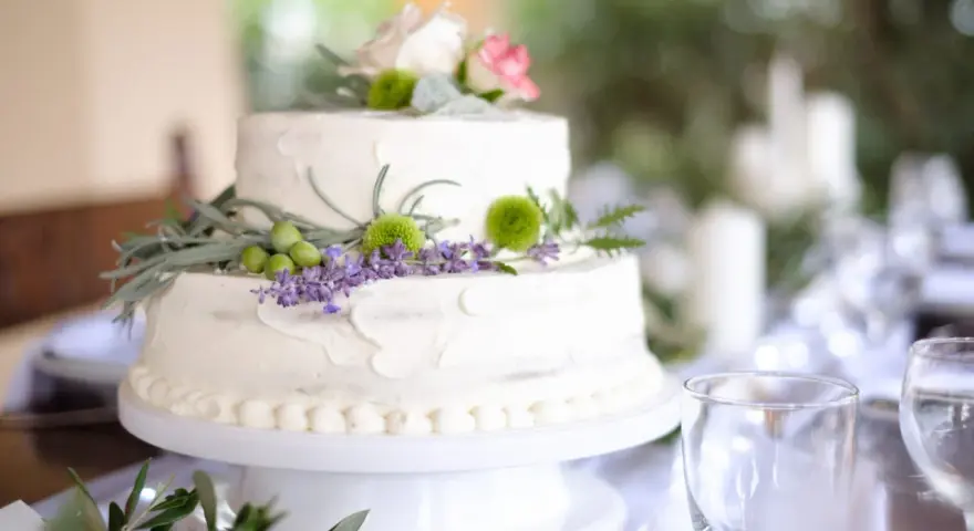 Dwupoziomowy tort weselny ozdobiony kwiatami, ziołami i oliwkami. Delikatne kremowe wykończenie i naturalne dekoracje podkreślają wyjątkowe smaki tortów weselnych.