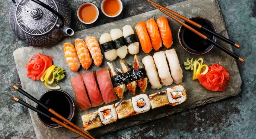 Piękny zestaw sushi: nigiri z łososiem, krewetkami, tuńczykiem i węgorzem, a także rolki. Obok czajniczek i filiżanki z herbatą. Idealne na co do sushi.