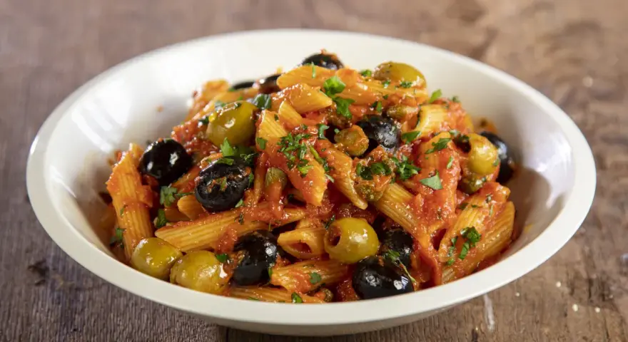 Penne con sugo rosso, olive nere e verdi, capperi e prezzemolo. Un piatto di pasta alla puttanesca invitante e saporito.