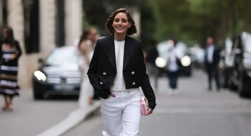 Mujer sonriente con chaqueta negra y pantalones blancos, lista para una comida familiar de invierno.