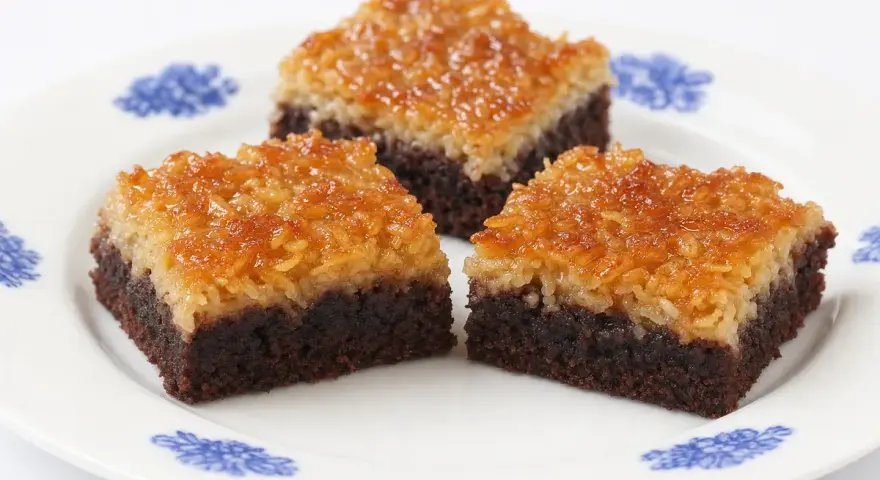 Chokladkakor med kokostosca, perfekta att baka i långpanna. Tre bitar på en vit tallrik med blått mönster.