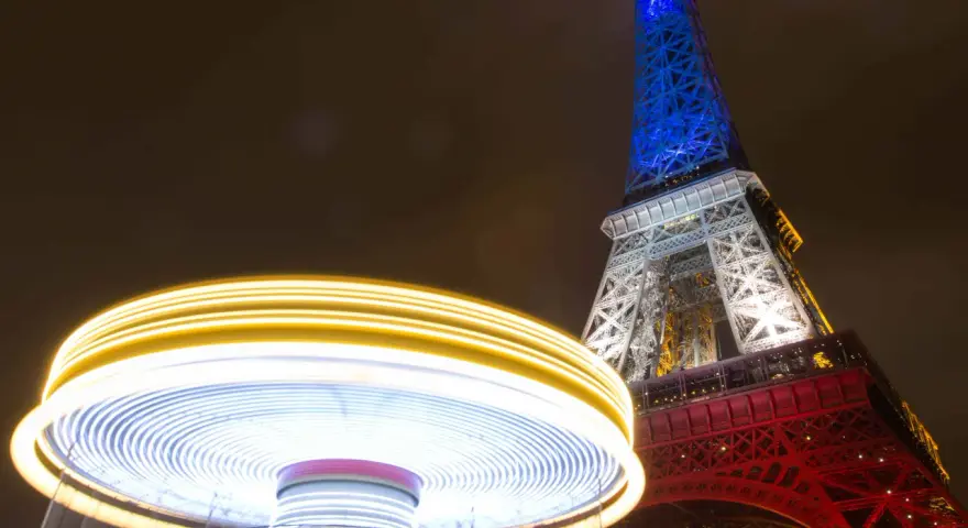 Manège lumineux tournant devant la Tour Eiffel illuminée en bleu, blanc et rouge. Une scène de Paris nocturne, parmi les plus belles photos de nuit.