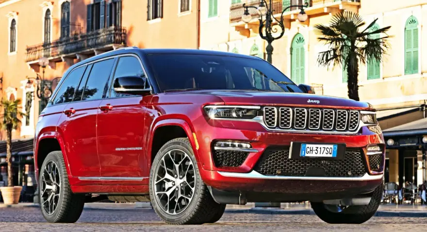 Czerwony Jeep Grand Cherokee zaparkowany na brukowanej ulicy przed budynkami z balkonami.