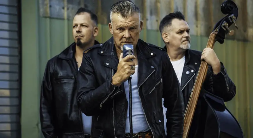 Rock n roll band in Lederjacken. Sänger hält Mikrofon, Bassist spielt Kontrabass, Schlagzeuger hält Sticks.