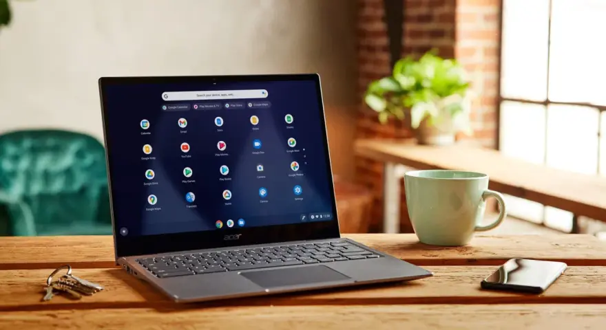Laptop z systemem Chrome OS Flex na drewnianym stole, obok kubek i klucze.