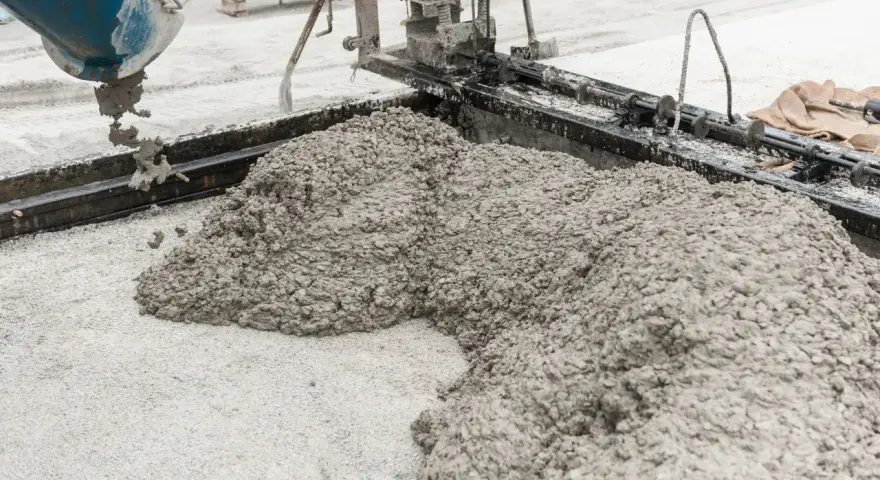 Beton wylewany z betoniarki na podłoże z drobnego kruszywa. Widać formę do wylewania betonu i masę, która tworzy kopiec.