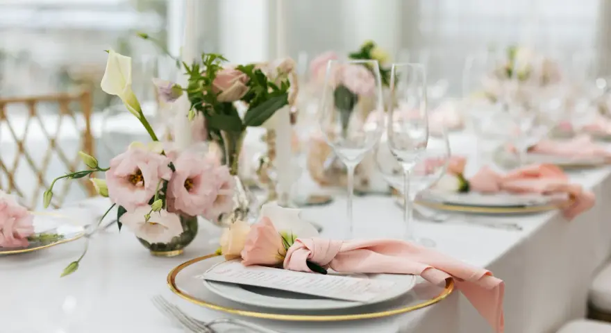Ett vackert dukat bord med rosa dekorationer, blommor och glas. En elegant dukning för ett speciellt tillfälle.