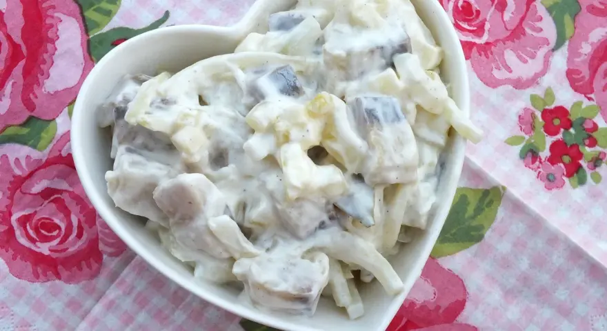 Pyszne matiasy w śmietanie z cebulą i ogórkiem, podane w sercowatej miseczce na różowej, kwiecistej serwetce.