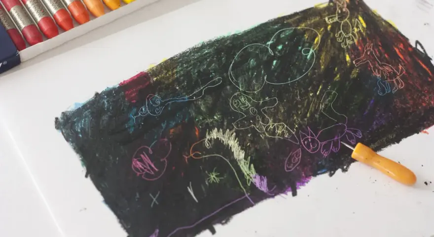 Un niño empieza a dibujar con ceras sobre un papel negro, revelando colores vibrantes y figuras fantásticas.