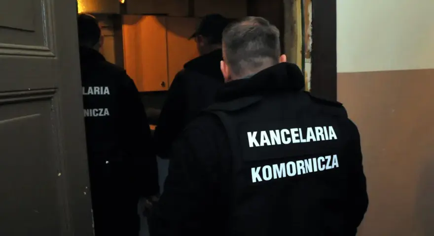 Komornicy w kamizelkach z napisem "KANCELARIA KOMORNICZA" wchodzą do pomieszczenia. Pytanie o alimenty na dziecko ile procent z wynagrodzenia może być związane z ich pracą.