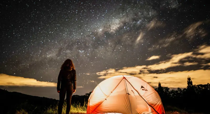 Nuit étoilée sur un bivouac GR34. Une personne admire la Voie lactée près d'une tente illuminée.