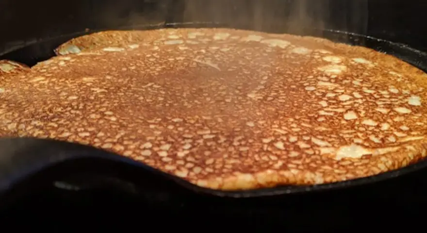 En gyllene, nygräddad pannkaka steker i en gjutjärnspanna. Perfekt för en glutenfri frukost eller fika.