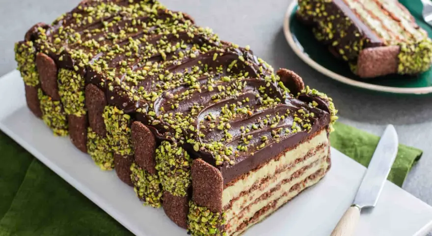 Torta fredda con strati di biscotti, crema e cioccolato, decorata con granella di pistacchio. Un tripudio di dolci al pistacchio.