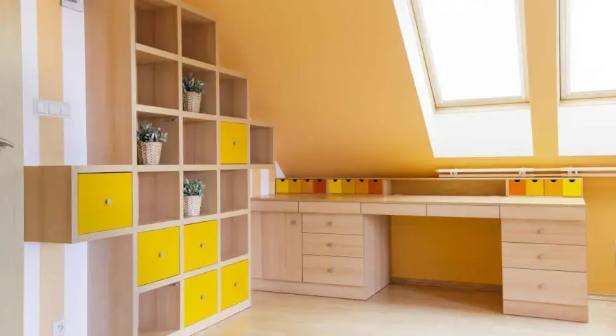 Luminosa mansarda con pareti arancioni e mobili in legno chiaro. Le idee colori pareti mansarda sono valorizzate da cubi contenitori gialli e un'ampia scrivania.