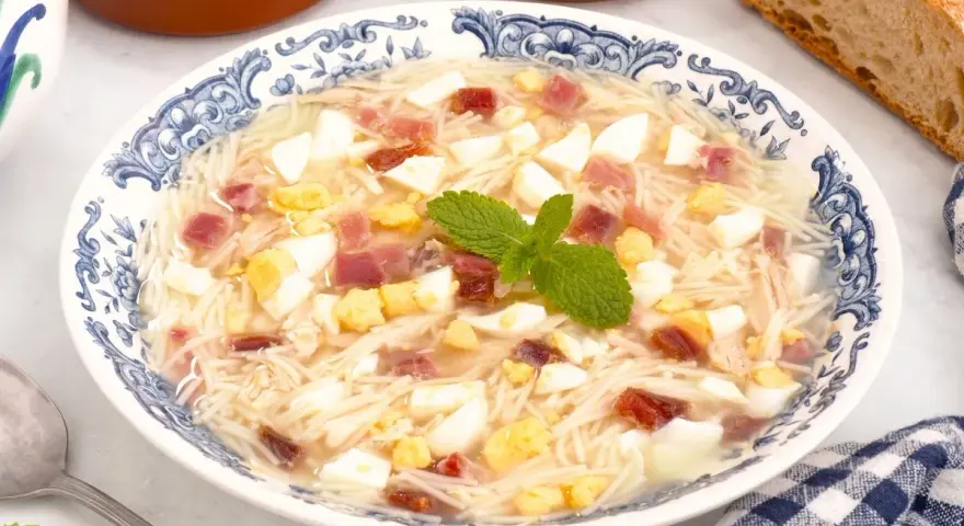 Sopa de picadillo andaluza en un plato azul y blanco con trocitos de huevo duro, jamón y fideos finos.