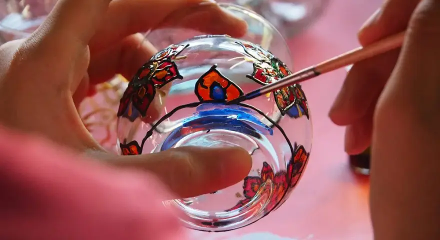 Manos pintando un vaso de cristal con flores de colores. Aprende como pintar cristal a mano y crea arte.