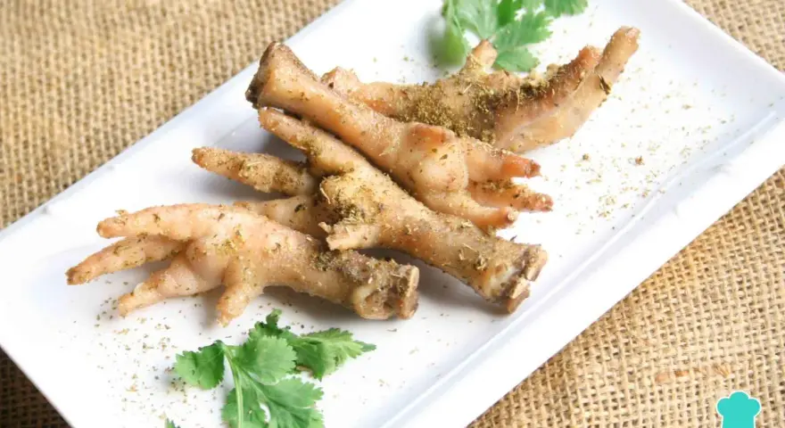 Patas de pollo sazonadas y listas para cocinar, adornadas con cilantro fresco sobre un plato blanco.