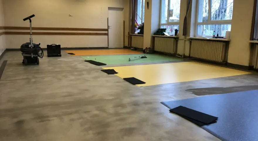 Przygotowanie podłogi pod wykładzinę PCV: odkurzacz przemysłowy i kolorowe maty czekają na ułożenie.