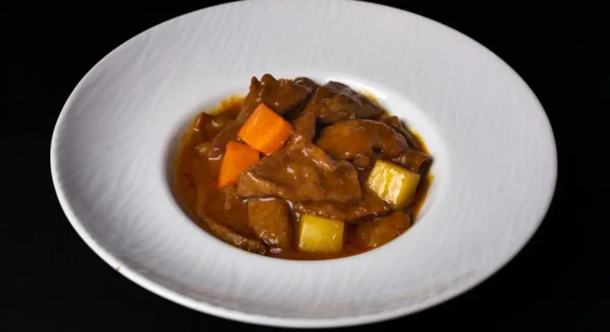 Estofado de carne con trozos de zanahoria y patata en una salsa espesa, servido en un plato blanco.