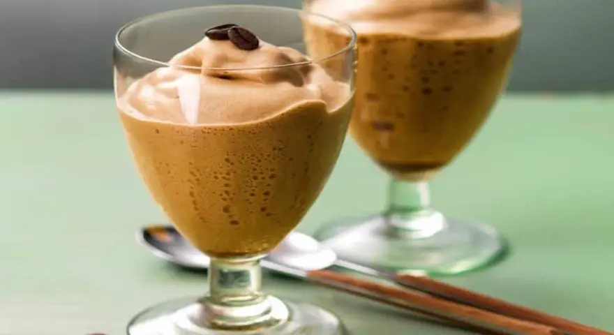 Due bicchieri di spumone al caffè, guarniti con chicchi di caffè, su un tavolo verde.