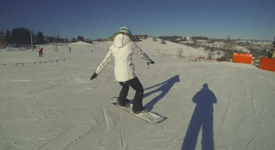 Osoba na snowboardzie na stoku narciarskim, ucząca się w szkole narciarskiej Budzyńskich. Słoneczny dzień, czyste niebo.