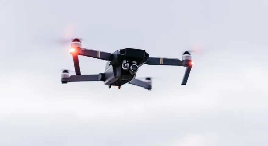 A drone hovers in the sky, its red lights blinking. Planning a trip? Be aware of Bahamas drone laws before you fly.