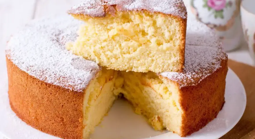 Una soffice torta fredda allo yogurt, spolverata di zucchero a velo, con una fetta sollevata che ne rivela la morbidezza.