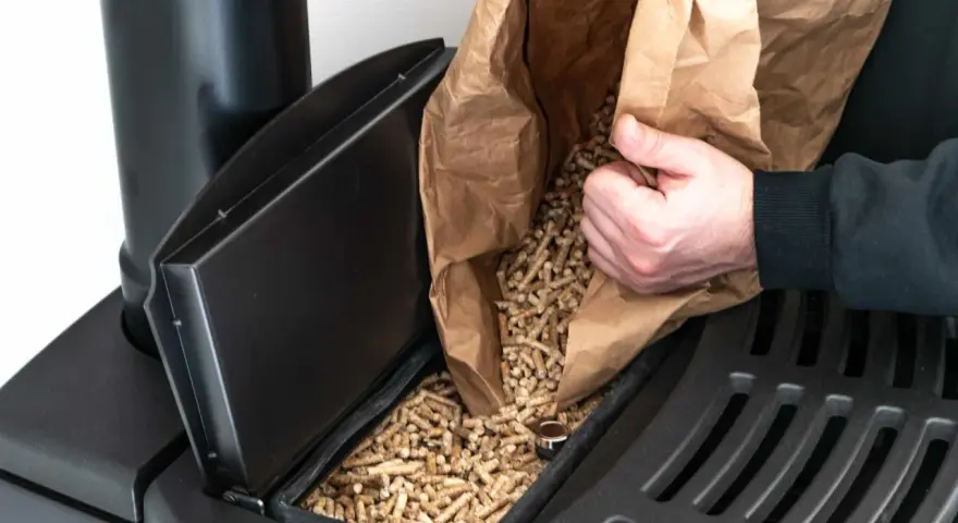 Persona rellena un compartimento de estufa de pellets. Considera el instalar estufa pellets precio para un hogar eficiente.