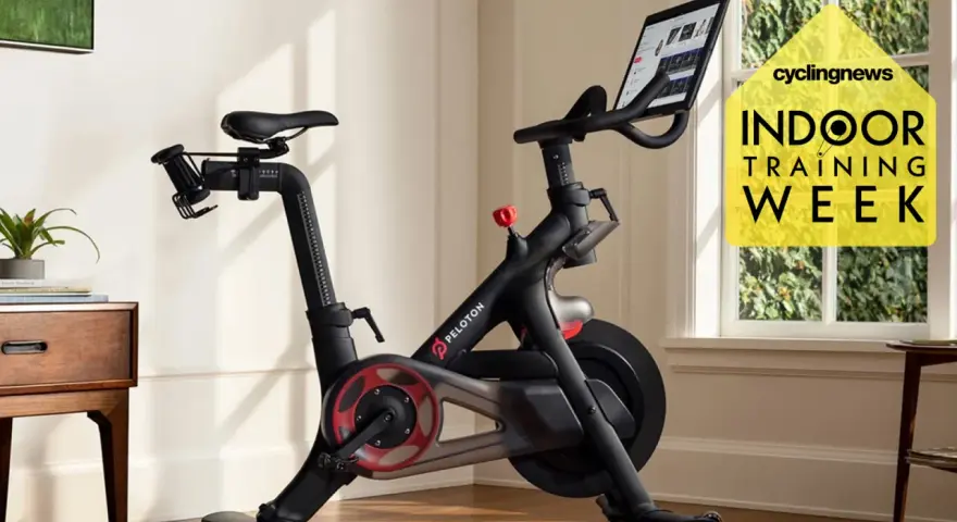 A Peloton bike, perfect for indoor cycling vs spinning, sits in a bright room. A yellow graphic promotes "Indoor Training Week.