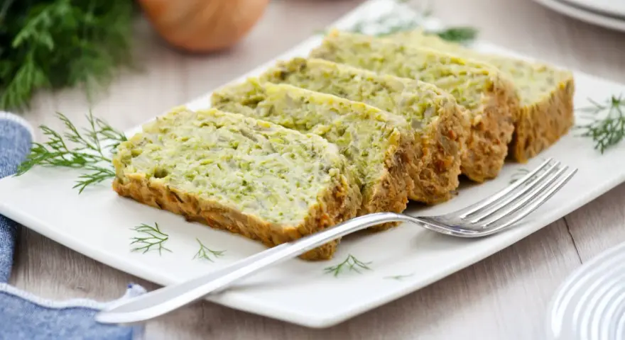Fette di flan di zucchine su un piatto bianco, guarnite con aneto. Una forchetta argentata è appoggiata sul piatto.