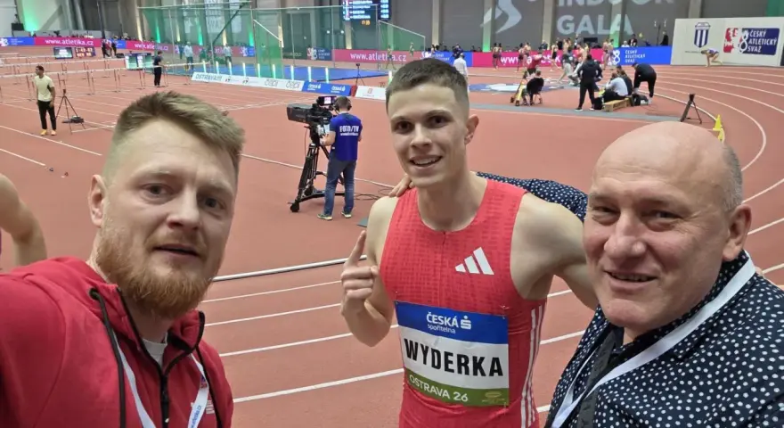Trzej mężczyźni na bieżni lekkoatletycznej. W środku zawodnik Maciej Wyderka w stroju sportowym.