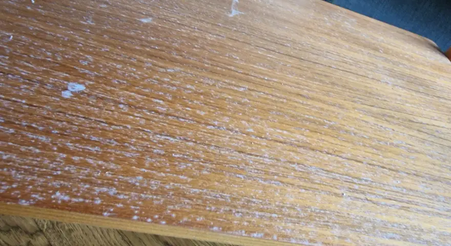 Detaljerad bild av en sliten teakskiva, redo för att renovera teakbord. Vita fläckar och repor syns tydligt.