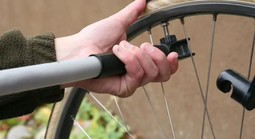 Dłoń trzyma pompkę rowerową, przygotowując się do sprawdzenia, jakie ciśnienie w oponach jest optymalne.