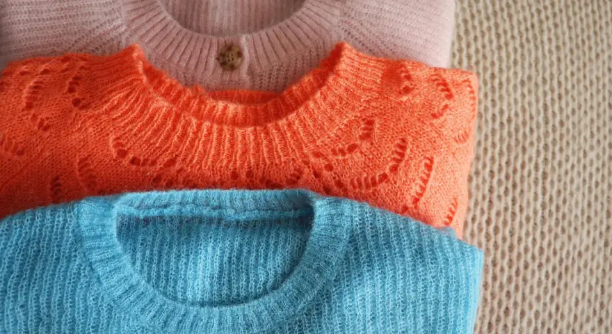 Gestapelte Pullover in Rosa, Orange und Blau. Zeit für die **Wolle waschen**, damit sie wieder flauschig sind.