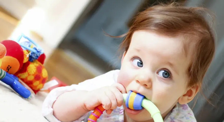 Bébé curieux mordillant un jouet coloré, dans le cadre d'un projet d'accueil individualisé pour son développement.