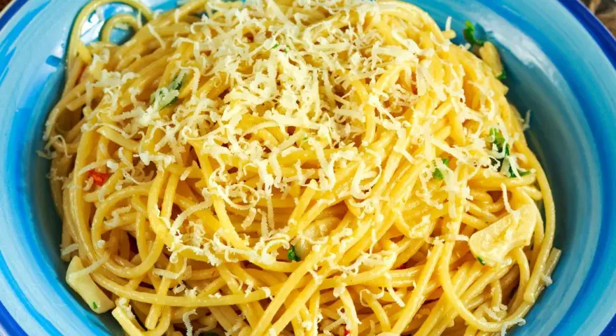 Porcja spaghetti z tartym serem i ziołami w niebieskiej misce.