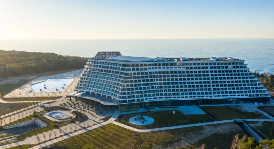 Nowoczesny, falisty pobierowo nowy hotel z basenami i widokiem na morze, otoczony lasem.