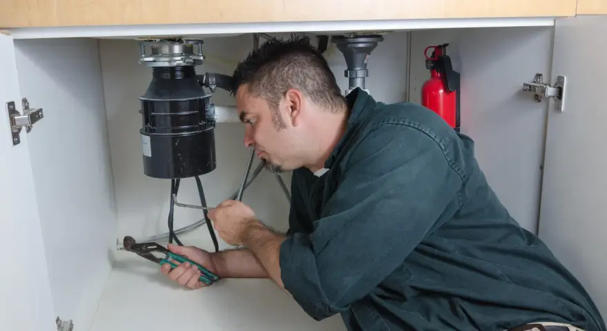 Man with pliers working on a garbage disposal under a sink.
