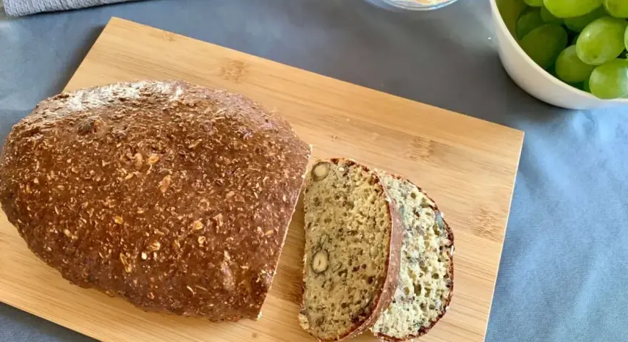 Chleb z twarogu na desce, pokrojony w kromki, obok miseczka z winogronami. Idealny przepis na chleb z twarogu.