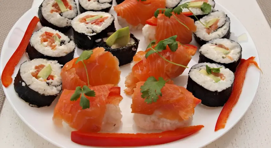 Piękne sushi kompozycje na białym talerzu: rolki z łososiem, awokado i papryką, ozdobione kolendrą.