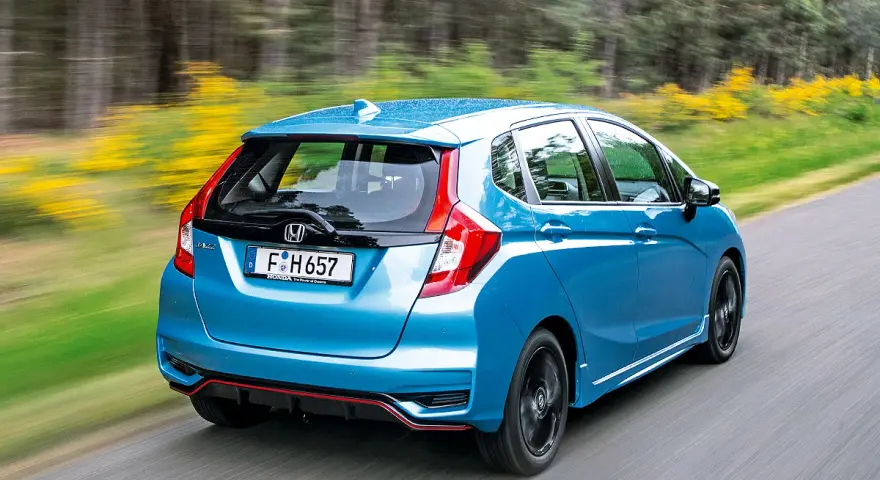 Blauer Honda Jazz Hybrid fährt auf einer Landstraße. Trotz der schönen Fahrt gibt es Berichte über Honda Jazz Hybrid Probleme.