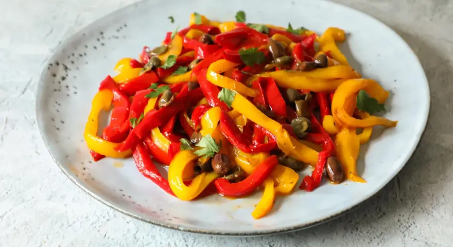 Peperoni in padella, tagliati a listarelle rosse e gialle, conditi con olive e capperi, guarniti con prezzemolo fresco.