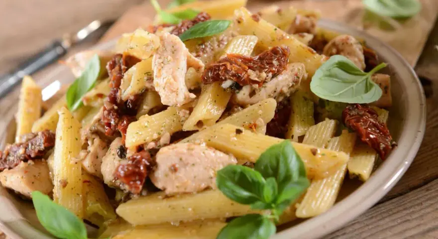 Penne z kurczakiem i suszonymi pomidorami, ozdobione świeżą bazylią. Pyszne danie na obiad.
