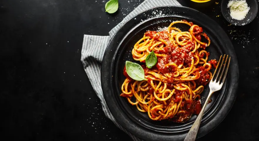 Un piatto di spaghetti alla carrettiera fumanti, conditi con un ricco sugo di pomodoro e basilico fresco, su sfondo scuro.