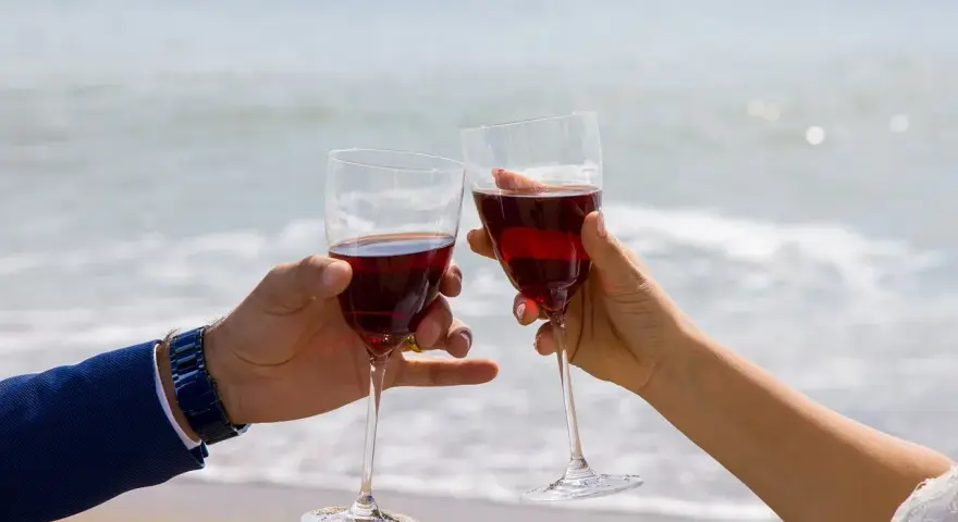 Dwie ręce unoszą kieliszki z czerwonym winem na tle morza. Idealne drinki z winem na romantyczny wieczór.