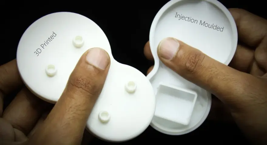 Hands hold two white plastic parts, one labeled "3D Printed" and the other "Injection Moulded," showcasing the difference between the two manufacturing methods.