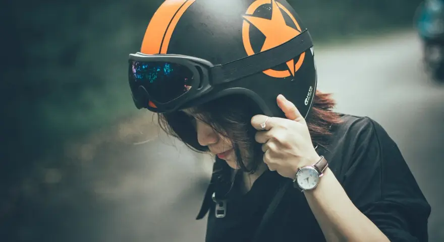 Donna con casco nero e arancione, occhiali riflettenti. Il casco deve calzare bene per la sicurezza.