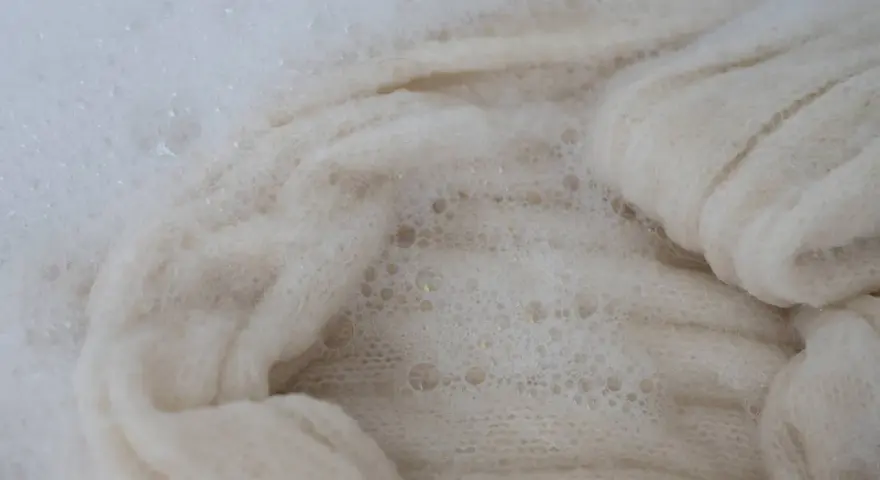 Lana bianca in acqua saponata, un processo che porta all'infeltrimento della lana per creare texture uniche.